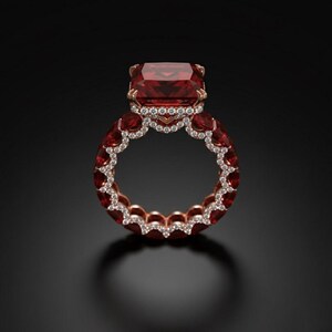 May include: A luxurious rose gold ring featuring a large, rectangular, deep red gemstone as the centerpiece. The band is adorned with smaller red gemstones and a row of sparkling white diamonds, creating a dazzling display of light and color.