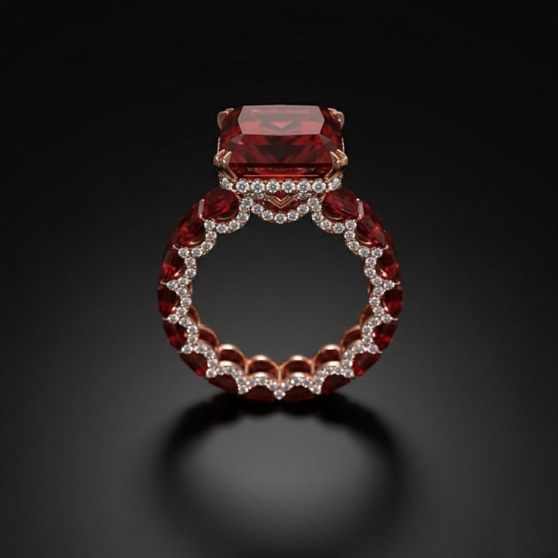 May include: A luxurious rose gold ring featuring a large, rectangular, deep red gemstone as the centerpiece. The band is adorned with smaller red gemstones and a row of sparkling white diamonds, creating a dazzling display of light and color.