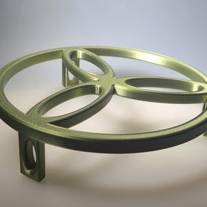 May include: A gold-colored, circular decorative stand with a three-petal design. The stand has a raised edge and is supported by three legs. The design is modern and geometric, suitable for displaying decorative items.