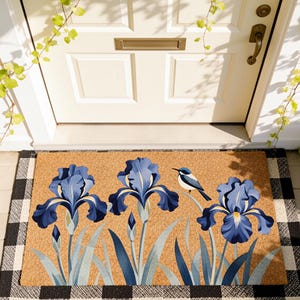 Può includere: Un zerbino rettangolare con un design botanico. Presenta tre fiori di iris blu e un piccolo uccello blu. Il tappeto ha uno sfondo marrone e un bordo a scacchi bianco e nero. È posto davanti a una porta bianca.