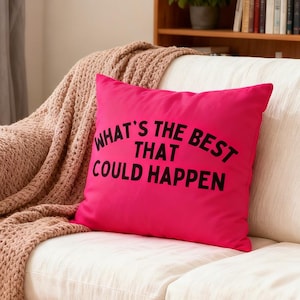 Puede incluir: Un cojín cuadrado rosa brillante con el texto negro "WHAT'S THE BEST THAT COULD HAPPEN". El cojín está sobre un sofá blanco con una manta de punto beige.
