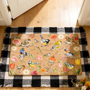 Puede incluir: Una alfombra rectangular con una ilustración detallada de pájaros coloridos en ramas con flores. La alfombra tiene un fondo beige y un borde a cuadros blanco y negro. Los pájaros incluyen azul, amarillo, naranja y marrón.