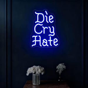 Puede incluir: Un letrero de neón azul que muestra las palabras "Die Cry Hate" en una fuente estilizada. El letrero está montado en una pared azul oscuro. Debajo del letrero, un jarrón con flores blancas y un jarrón pequeño con flores blancas están sobre una superficie de madera.