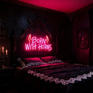 Puede incluir: Un dormitorio oscuro con una cama de estilo gótico con un letrero de neón que dice "Born With Horns". La cama tiene un edredón negro con ribete de encaje blanco. La habitación está iluminada con luz de neón roja.