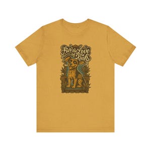 May include: Mustard yellow t-shirt featuring a cartoon dog smoking a cigarette, with the text "Fur the Love of Kush." The dog is sitting on a decorative chair, surrounded by cannabis leaves. The design is in shades of brown, green, and cream.