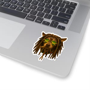 May include: A sticker depicting a dog with brown dreadlocks, wearing sunglasses with the Jamaican flag design. The dog also has a beaded necklace. The sticker is on a laptop.
