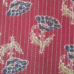 Könnte beinhalten: Nahaufnahme eines roten Stoffes mit floralem Muster. Das Design zeigt stilisierte Blumen in Marine-, Braun- und Beigetönen, vor einem Hintergrund aus vertikalen weißen gepunkteten Linien. Der Stoff hat ein strukturiertes Aussehen, was auf ein gewebtes oder bedrucktes Textil hindeutet.