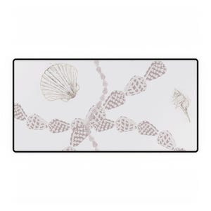 Puede incluir: Una bandeja decorativa rectangular blanca con borde negro. La bandeja presenta ilustraciones de conchas marinas y una cadena de conchas en tonos grises y taupe, creando un tema costero.