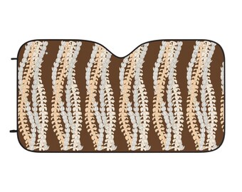 May include: A car sunshade with a brown background and a repeating pattern of vertical, stylized floral designs in white and beige. The sunshade has a curved top edge and black tabs on the sides.