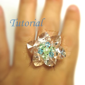 May include: A crystal flower ring with green and blue beads. The ring is on a hand, and the word "Tutorial" is written above the ring.