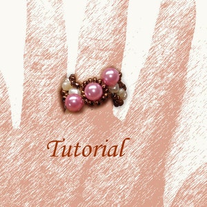 Op de afbeelding: Een roze en witte kralenring met een tutorial-tekst eroverheen. De ring is gemaakt van kleine ronde kralen en grotere roze kralen.