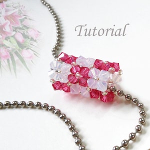 May include: A silver chain necklace with a pink and white beaded pendant. The pendant is made of small, faceted beads that are arranged in a flower-like pattern. The word "Tutorial" is written in cursive on the white background.