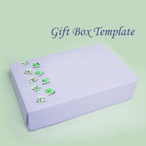 May include: A lavender gift box template with a row of green and brown floral accents. The box is rectangular and has a lid. The words "Gift Box Template" are written in dark blue script.