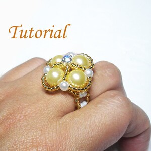 May include: A gold ring with a flower design made of white and yellow beads. The center of the flower has a clear rhinestone.