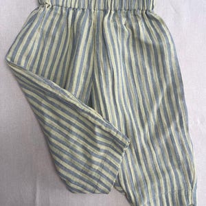 May include: Blue and yellow striped trousers with an elasticated waistband. The trousers are made of a lightweight fabric, suitable for casual wear. The vertical stripes create a visually appealing pattern.