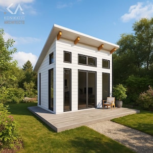 May include: A modern, white cabin with a sloped roof and large black-framed windows and doors. The cabin has a wooden deck and is surrounded by green grass and trees. A small chair sits on the deck.