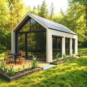 May include: A modern, light-colored cabin with a gabled roof and large glass windows. The cabin features a wooden deck with a table and chairs, surrounded by a garden and lush green grass. The cabin is set in a wooded area.