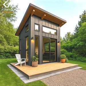 Puede incluir: Una pequeña casa moderna, de color gris oscuro, con una terraza de madera y un tejado inclinado. La casa tiene grandes ventanas y una puerta corredera de cristal. Una silla blanca y plantas en macetas están en la terraza. La casa está rodeada de hierba verde y árboles.