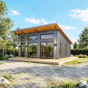 May include: A modern, gray-sided cabin with a wooden deck and a sloped roof. Large windows and glass doors offer views of the surrounding trees. The cabin has a natural wood overhang and is set against a blue sky.