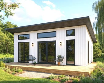 May include: A modern white cabin with a dark brown roof and black window frames. The cabin has a wooden deck with two chairs and a small table. The cabin is surrounded by green grass and trees.