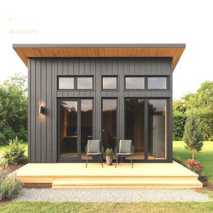 Può includere: Un moderno capannone grigio scuro con un ponte di legno e una piccola area di ghiaia. Il capannone ha grandi porte e finestre di vetro, con due sedie e una pianta in vaso sul ponte. Il testo "ARCHITECTS" è visibile nell'angolo in alto a sinistra.