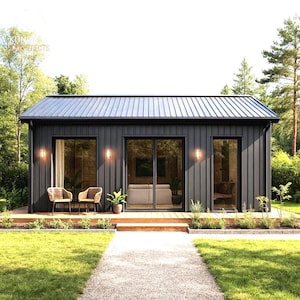 Op de afbeelding: Een moderne, donkergrijze cabine met een metalen dak, grote ramen en een houten terras. Twee rieten stoelen staan op het terras. De cabine is omgeven door een groen gazon en bomen, met een grindpad dat naar de ingang leidt.