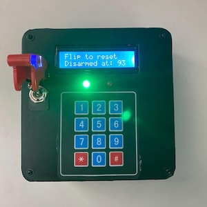 Pode incluir: Um teclado eletrônico preto com uma tela LCD azul exibindo "Flip to reset. Disarmed at: 93." Uma chave vermelha é inserida em uma fechadura à esquerda. O teclado possui botões numerados e uma luz verde.