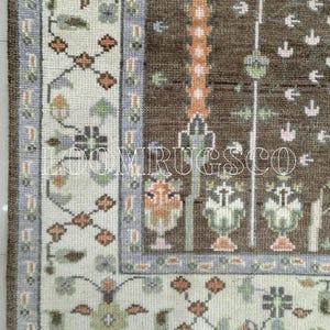 May include: Detail of a brown and cream rug with a complex design. The rug has a central brown section with vertical floral patterns and a cream border with geometric and floral elements. The text "LOOMIRUGS CO" is visible.