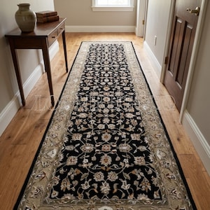 May include: A long rectangular runner rug featuring a black central field with a dense, symmetrical floral pattern in shades of cream, tan, and brown. The rug is framed by a wide, decorative border in a muted olive-tan tone with floral motifs.