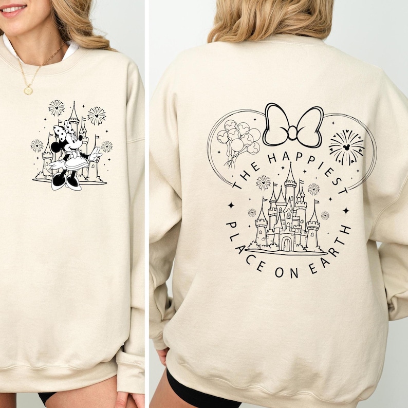 Może przedstawiać: Kremowa bluza z czarno-białą grafiką Myszki Minnie, zamkiem i fajerwerkami. Tył bluzy przedstawia zamek, kokardę, balony i napis "THE HAPPIEST PLACE ON EARTH" w okręgu.