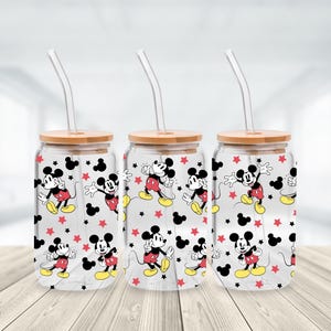 May include: Three clear glass tumblers with bamboo lids and glass straws. Each tumbler features a repeating pattern of Mickey Mouse, red stars, and black Mickey Mouse silhouettes. The tumblers are on a light wood surface.