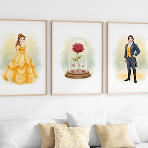 May include: Three framed art prints featuring watercolor illustrations. One shows a woman in a yellow gown, another a red rose in a glass dome, and the third a man in a blue coat. The prints are displayed above a white sofa.