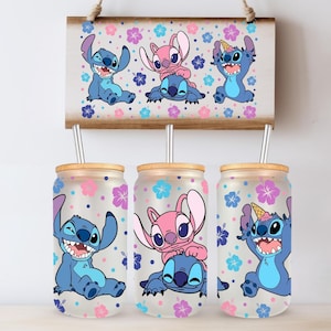 May include: Three glass tumblers with bamboo lids and straws, featuring cartoon characters Stitch and Angel. The tumblers have a floral pattern with pink, blue, and purple flowers. A matching wooden sign hangs above.