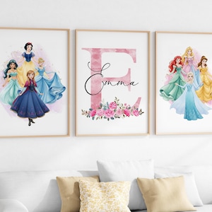 May include: Three framed art prints with watercolour illustrations. One print shows a pink letter "E" with the name "Emma" and floral accents. The other two prints feature Disney princesses in their iconic gowns, including Snow White, Elsa, and Ariel.