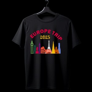 Puede incluir: Camiseta negra con un gráfico colorido de monumentos europeos, incluyendo la Torre Eiffel y el Big Ben. El texto "EUROPE TRIP 2025" está arqueado sobre el diseño del horizonte. La camiseta se muestra en una percha negra.