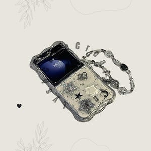 Puede incluir: Una funda plateada para teléfono con borde ondulado, decorada con estrellas de purpurina, corazones y una correa transparente con cuentas. La pantalla del teléfono muestra la hora. Un accesorio decorativo.