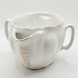 Puede incluir: Jarra de afeitar de cerámica blanca con dos asas y un borde festoneado. La jarra tiene una abertura lateral y letras doradas que dicen "MAIGRE". El borde y la abertura están adornados con oro.