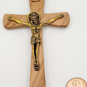 Può includere: Una croce di legno con una figura in bronzo di Gesù Cristo. La croce porta l'iscrizione "INRI". Una moneta è accanto alla croce per la scala. La croce è fatta di legno chiaro.