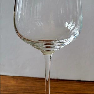 May include: A clear wine glass with a long stem and a wide bowl. The glass sits on a round base and is made of transparent glass. The glass is empty and reflects the light.
