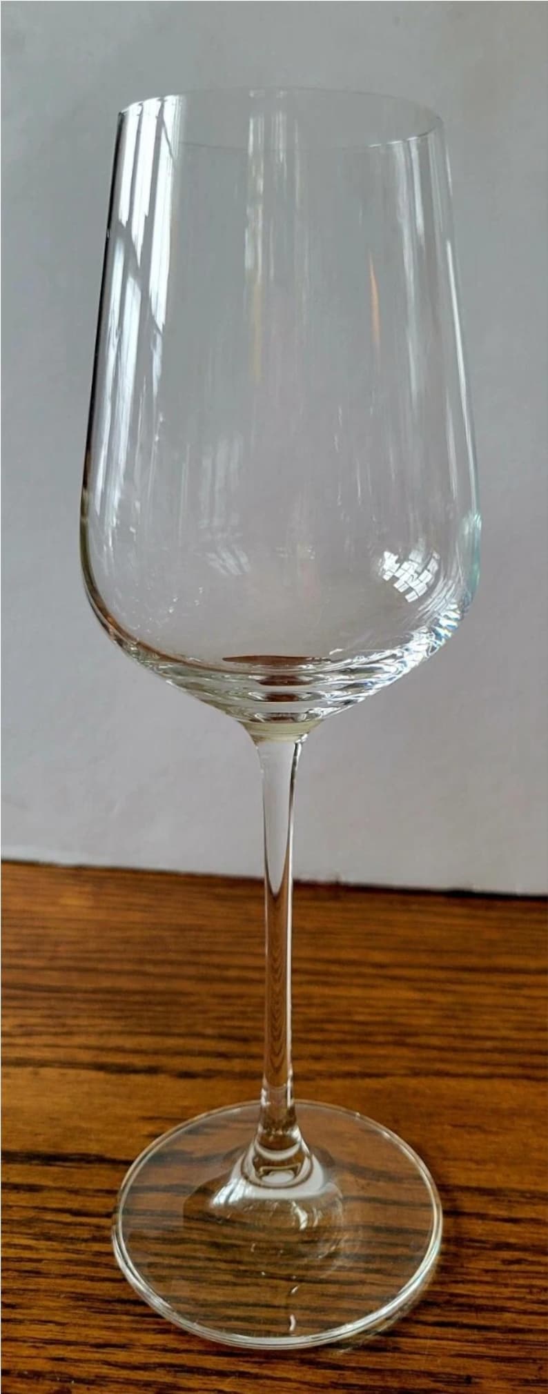 May include: A clear wine glass with a long stem and a wide bowl. The glass sits on a round base and is made of transparent glass. The glass is empty and reflects the light.