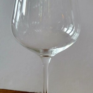 May include: A clear wine glass with a long stem and a wide bowl. The glass is made of transparent material, allowing light to pass through. The base is round and flat, providing stability. The glass is designed for serving wine.