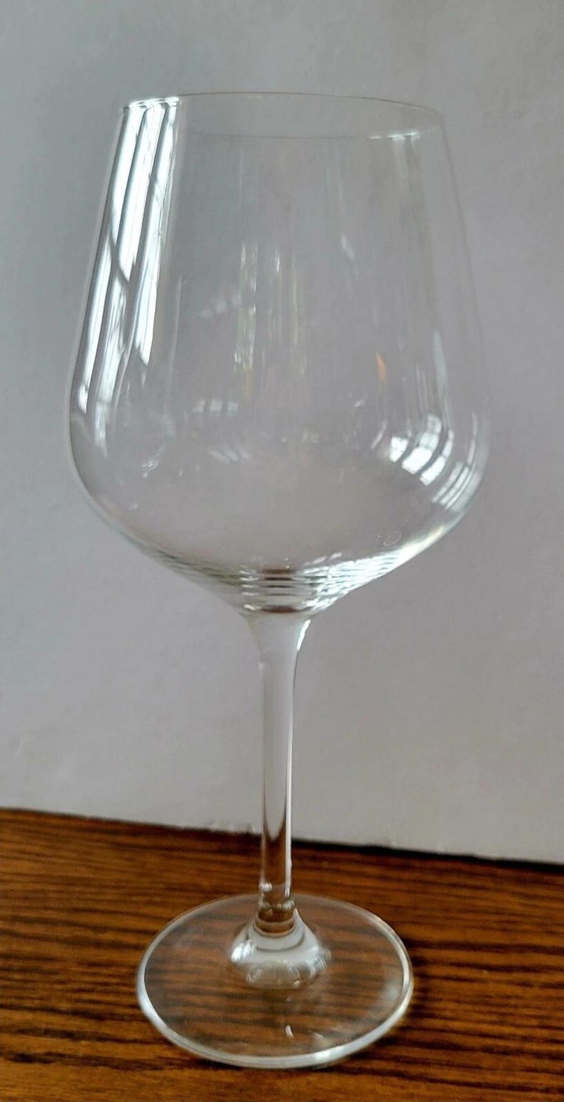 May include: A clear wine glass with a long stem and a wide bowl. The glass is made of transparent material, allowing light to pass through. The base is round and flat, providing stability. The glass is designed for serving wine.
