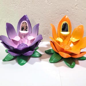 May include: Two decorative lotus flower sculptures. One is purple with pink and green accents, the other is orange with yellow and green accents. Each has a small mirror and two small shelves inside the flower.