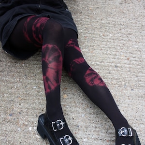 May include: Black tights with a red tie-dye pattern. The tights are worn with black platform sandals with silver buckles.