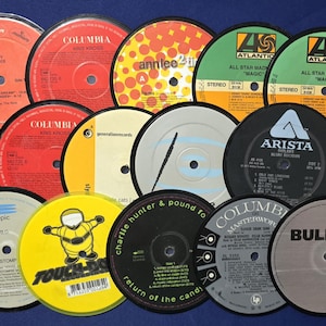 May include: A collection of twelve circular vinyl record labels in various colors including red, orange, yellow, green, black, and white. Each label features unique printed text, logos, and track listings from record labels like Columbia, Atlantic, and Arista.