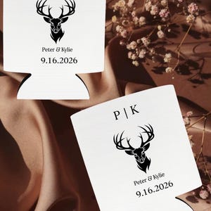 以下が含まれることがあります： 黒い鹿の頭のデザイン、イニシャル「P | K」、名前「Peter & Kylie」、日付「9.16.2026」がプリントされた白い缶クーラー2つ。背景は茶色です。