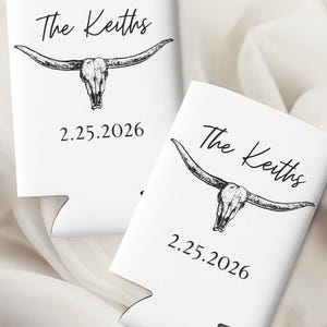 May include: Two white can coolers with a black longhorn skull design. The text "The Keiths" and the date "2.25.2026" are printed on the front. The coolers are for a wedding or event.