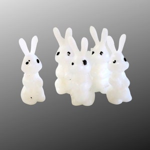 May include: Five white ceramic bunny figurines with black eyes. One bunny is standing alone, while the other four are clustered together.