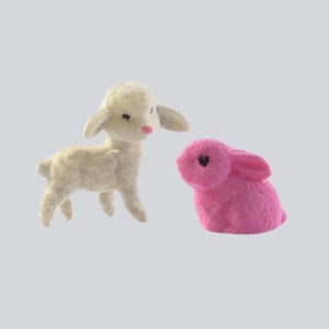 May include: A white fluffy lamb figurine with a pink nose and black eyes, standing next to a pink fluffy bunny figurine with black eyes.