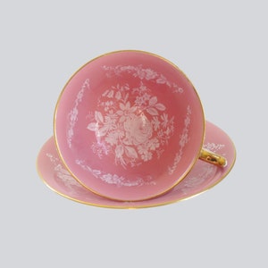 Vintage Pink Teacup and saucer with white roses similar to lace on the foreground of the cup and saucer all edged in gold leaf.  Https://swirlingorange11.etsy.com Swirlingo11.bsky.social
